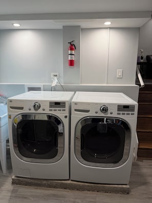 Two stacked front-loading washing machines in a laundry room with a fire extinguisher mounted on the wall.
