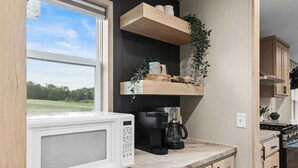 Een keuken met een magnetron, koffiezetapparaat en houten kastjes.