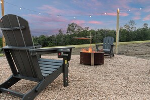 Zwei Adirondack-Stühle, ein Feuerkorb und Lichterketten im Außenbereich.