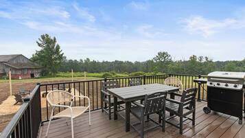 A wooden deck with a table and chairs, a grill, and a view of a barn and trees.
