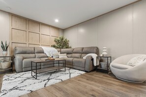 Uma sala de estar moderna com um sofá modular, uma mesa de centro redonda, uma poltrona branca e uma pequena mesa lateral.