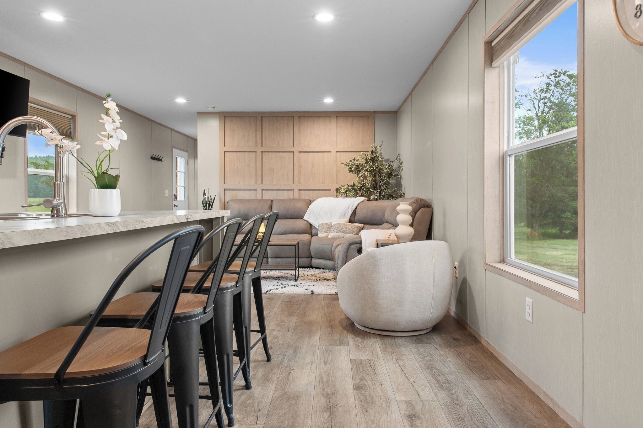 A modern kitchen with a dining area, built-in wooden cabinets, and a large window offering a view of the outdoors.