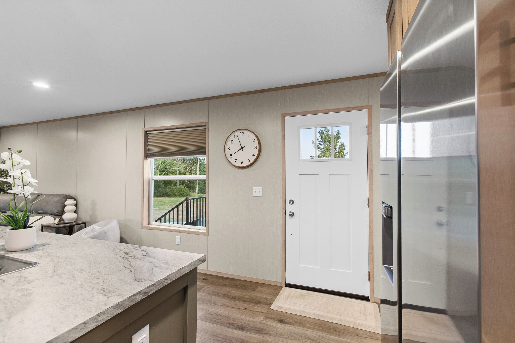 A modern kitchen with a marble countertop, a clock, a door, and a view of the outdoors.