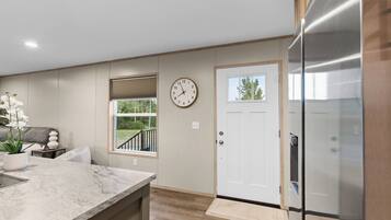 A modern kitchen with a marble countertop, a clock, a door, and a view of the outdoors.
