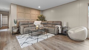 Een moderne woonkamer met een hoekbank, een salontafel, een bijzettafeltje, een vloerlamp en een fauteuil.