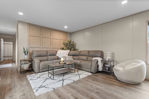 A modern living room with a sectional sofa, a coffee table, a side table, a floor lamp, and a chair. - Hot Tub Retreat on 190-Acre Farm · Sleeps 6 (Lakewood)