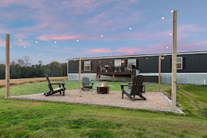 A backyard with a fire pit, outdoor seating, and a deck. - Hot Tub Retreat on 190-Acre Farm · Sleeps 6 (Lakewood)