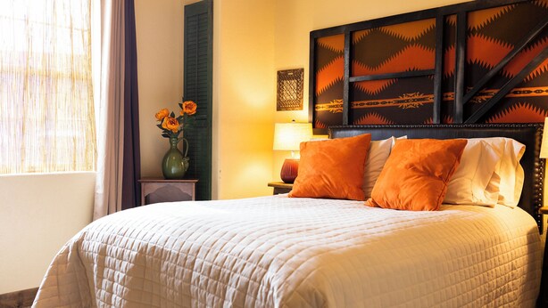 A hotel room with a large bed, a nightstand, a vase with flowers, and a wall with a decorative headboard. - Inn at Gard Estate Wines (Prosser)