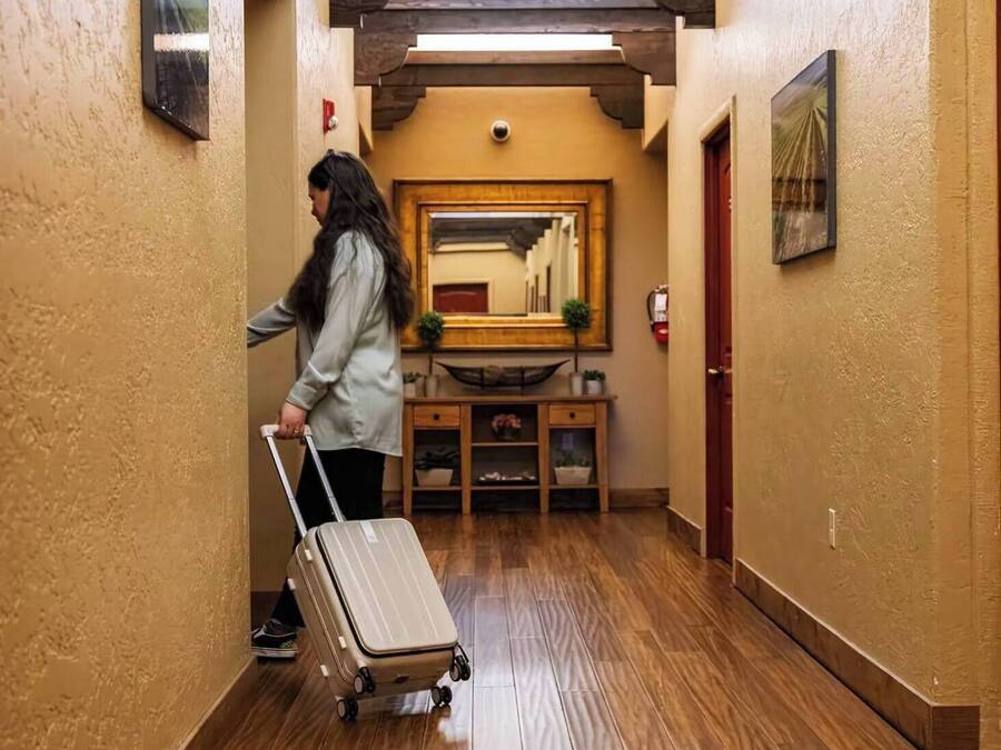 Un couloir étroit au plancher de bois, un banc en bois avec un miroir, et une porte au fond.