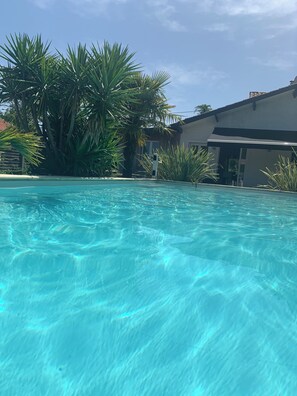 A clear swimming pool surrounded by tropical plants and a building with a flat roof. - Beautiful house nearby is operational (La Teste-de-Buch)