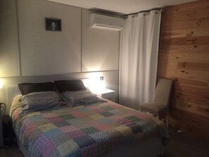 A bedroom with a bed, a bedside lamp, an air conditioner, a wooden wall panel, and a curtain. - Beautiful house nearby is operational (La Teste-de-Buch)