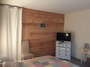 Ein Schlafzimmer mit einer Holzwand, einem Bett mit Decke, einem Fernseher auf einer Kommode und einem kleinen Tisch mit Bilderrahmen.
