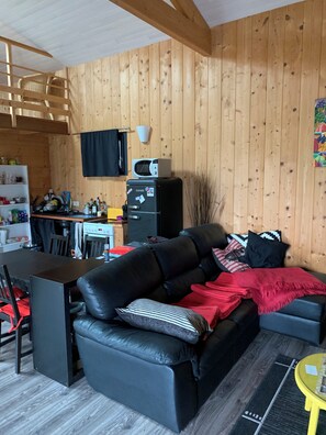 A cozy cabin interior with a wooden interior, a black leather sofa, a dining table, and a kitchen area with a microwave. - Beautiful house nearby is operational (La Teste-de-Buch)