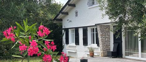 Une maison avec une façade en pierre, une terrasse en bois et un jardin agrémenté de fleurs roses.