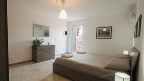 A bedroom with a bed, dresser, bedside lamp, and a view of the outside. - PENTHOUSE IN THE HEART OF DOGLIANI, LANGHEXPLORER (Dogliani)