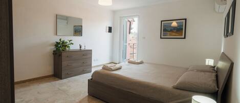 A bedroom with a bed, dresser, bedside lamp, and a view of the outside.