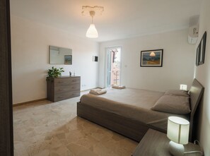 A bedroom with a bed, dresser, bedside lamp, and a view of the outside. - PENTHOUSE IN THE HEART OF DOGLIANI, LANGHEXPLORER (Dogliani)
