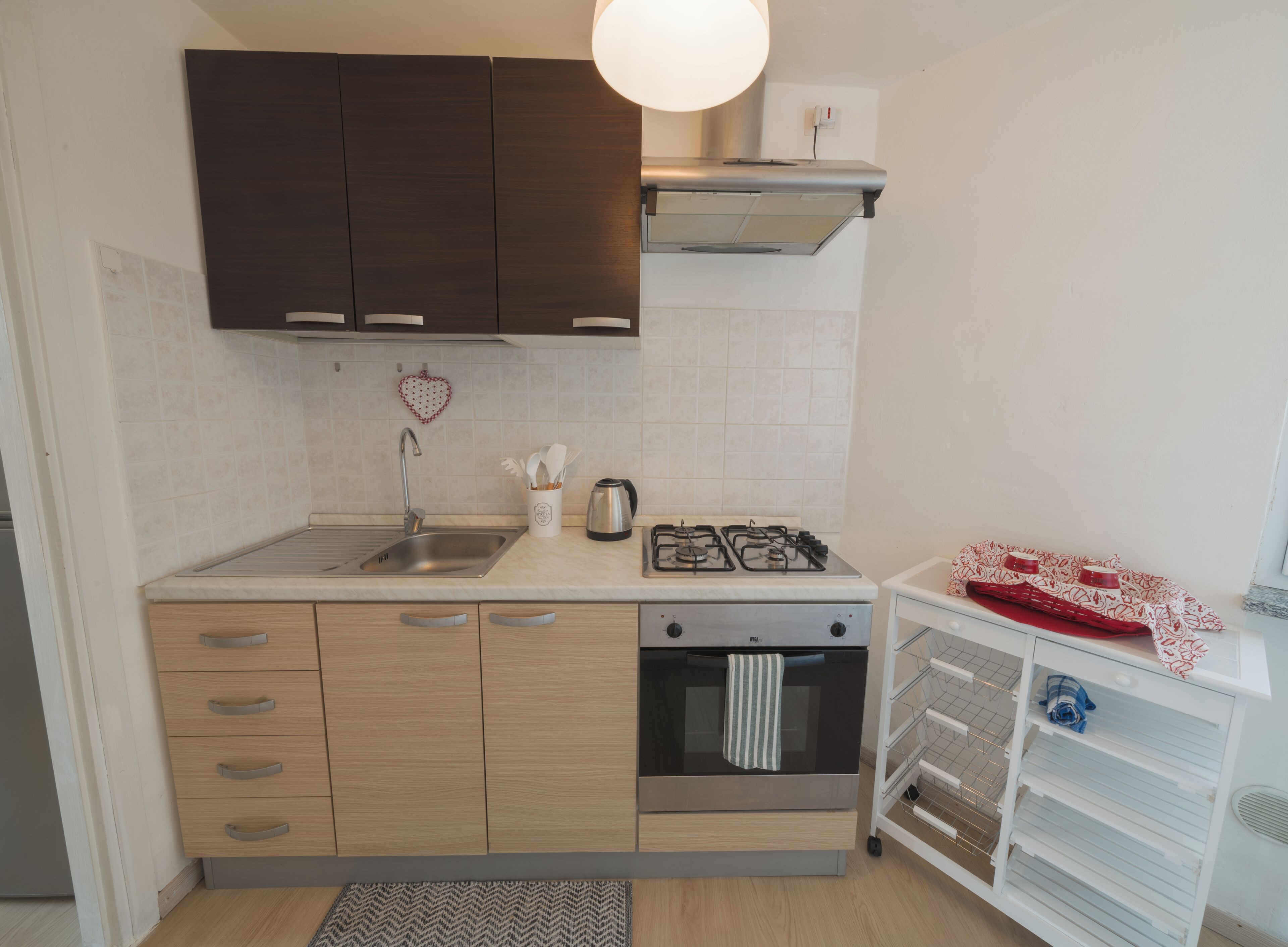 Une cuisine moderne dotée d’un évier en acier inoxydable, de meubles en bois, d’une cuisinière à gaz et d’un four encastré.