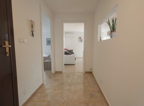 A hallway with a tiled floor, a door on the left, and a plant on the right. - PENTHOUSE IN THE HEART OF DOGLIANI, LANGHEXPLORER (Dogliani)