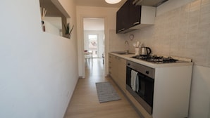 A modern kitchen with a gas stove, oven, and a small dining area visible through an open door. - PENTHOUSE IN THE HEART OF DOGLIANI, LANGHEXPLORER (Dogliani)