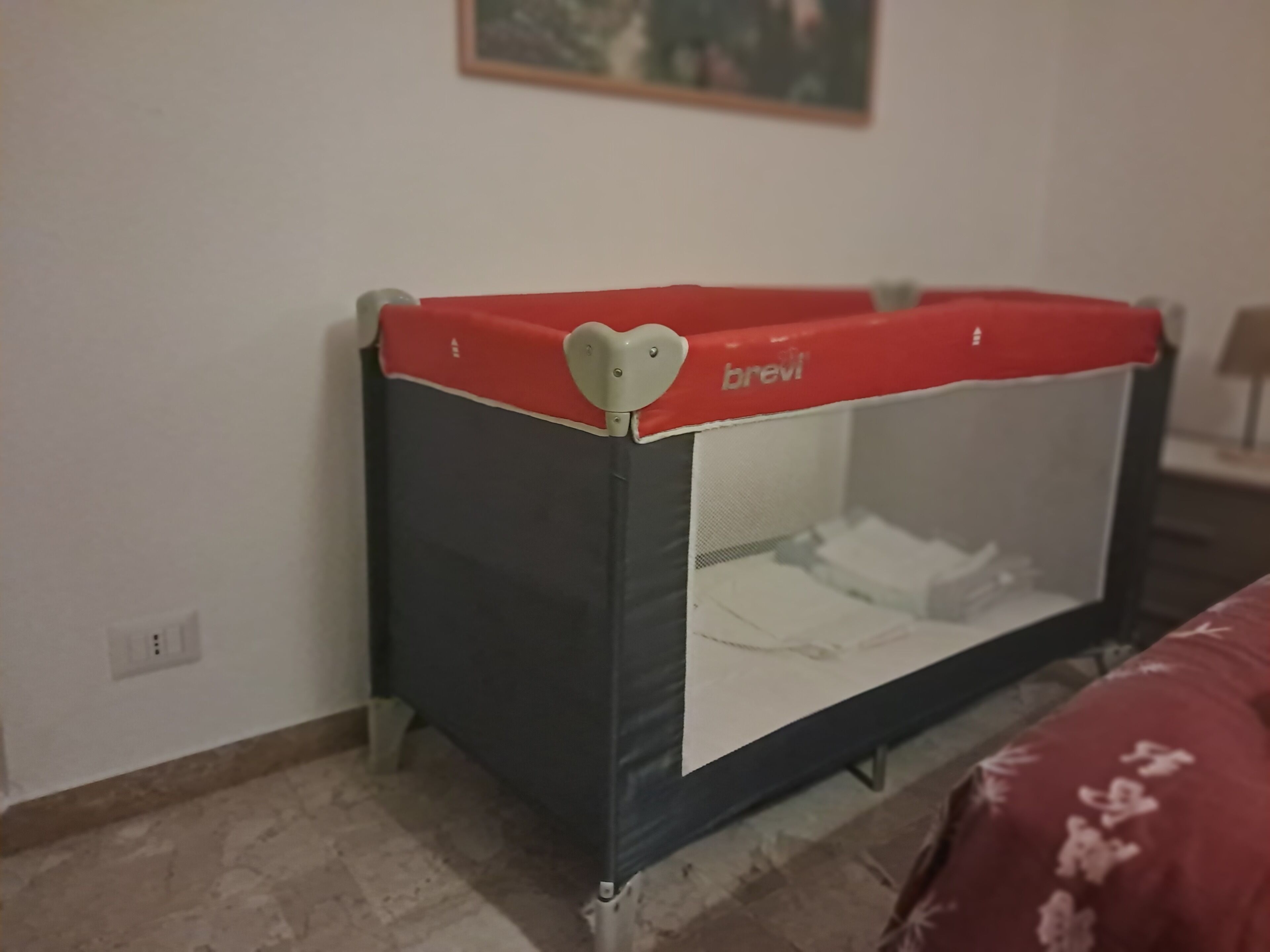 Una habitación con una cuna para bebé de color negro y rojo, un enchufe y un cojín estampado.