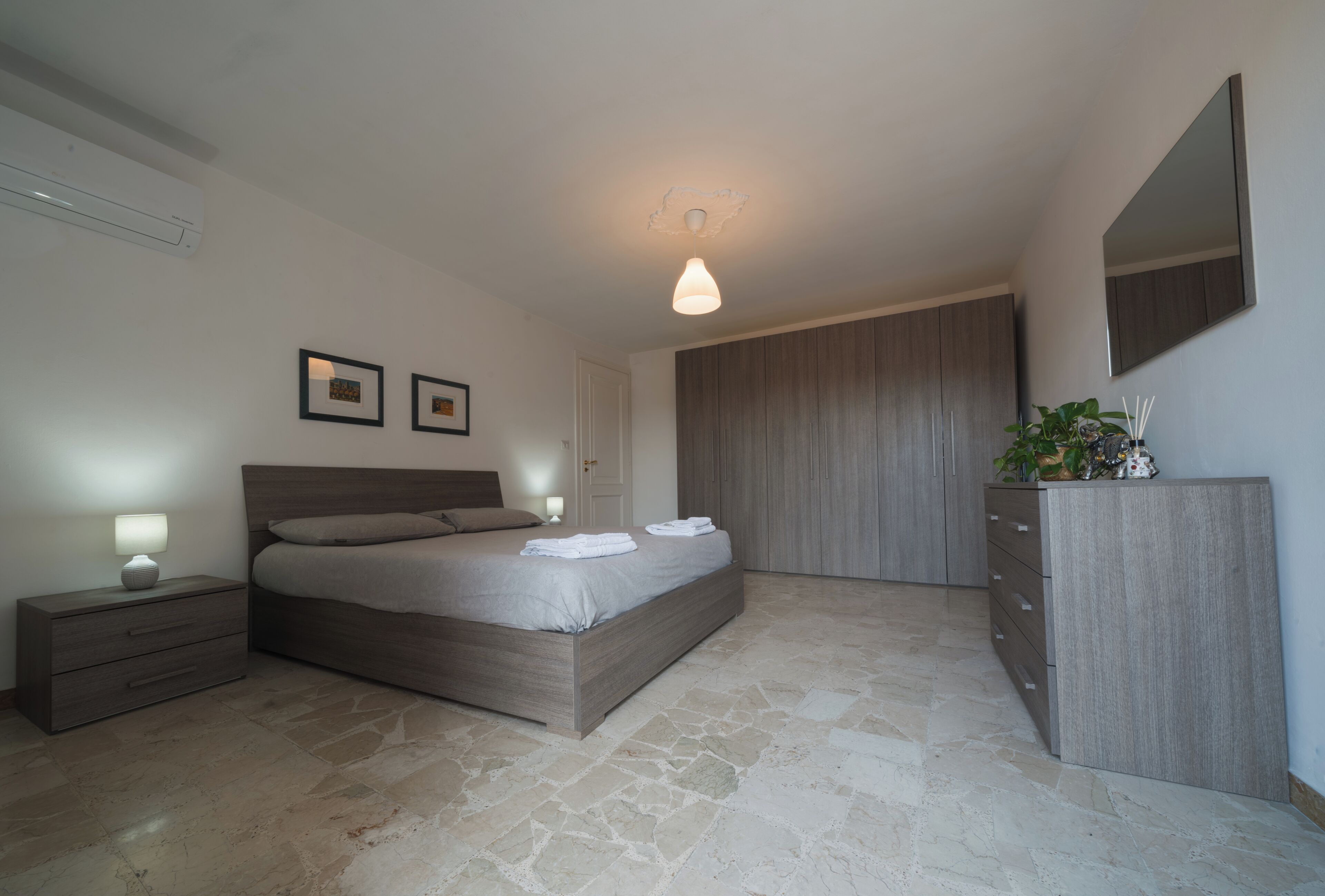 A modern bedroom with a large bed, bedside tables, a wardrobe, and a mirror.