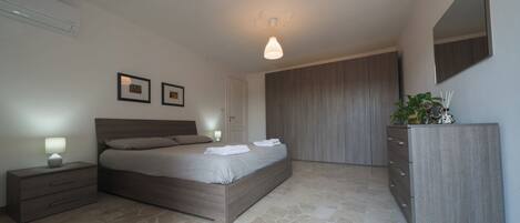 A modern bedroom with a large bed, bedside tables, a wardrobe, and a mirror.
