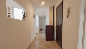 A hallway with a stone floor, a potted plant, a door with a security device, and a wall-mounted phone. - PENTHOUSE IN THE HEART OF DOGLIANI, LANGHEXPLORER (Dogliani)