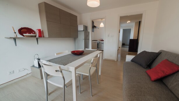 A modern kitchen with white cabinetry, a dining table with chairs, and a grey sofa with red cushions. - PENTHOUSE IN THE HEART OF DOGLIANI, LANGHEXPLORER (Dogliani)