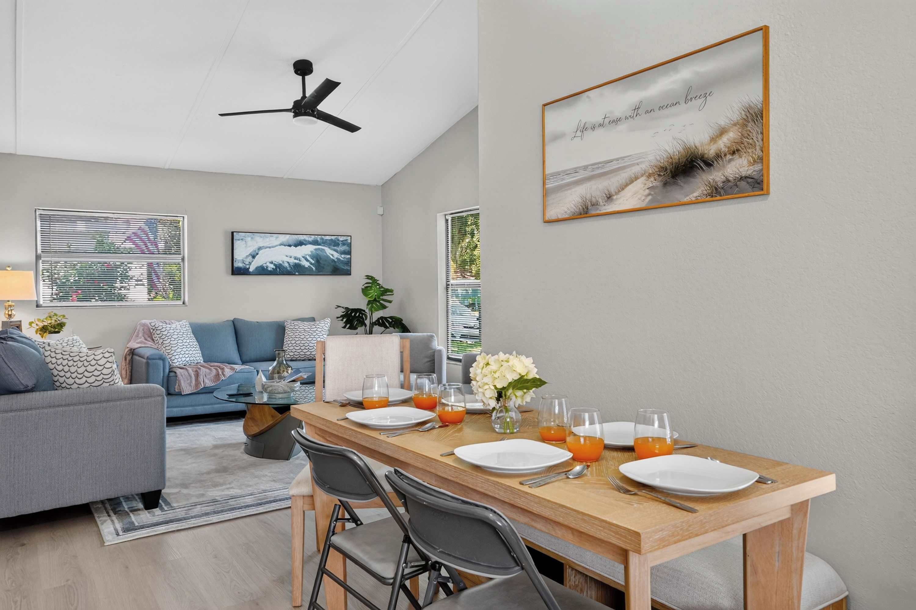 A modern living room with a dining area, featuring a ceiling fan, artwork, and a view of the outdoors.