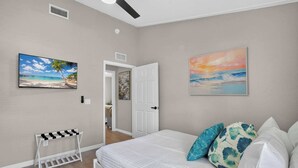 A bedroom with a bed, a door, a wall-mounted shelf, and a painting. - Modern Hacienda | 3BR, Fenced Yard, Beach Gear, Dog-Friendly, Near Downtown (Sarasota)