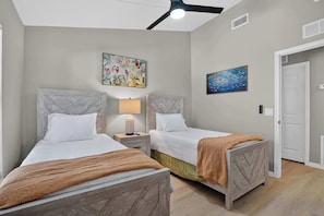 Ein Schlafzimmer mit zwei Betten, einem Deckenventilator und zwei an der Wand befestigten Bildern.