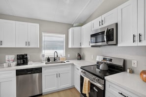 A modern kitchen with white cabinets, stainless steel appliances, and a window with blinds. - Modern Hacienda | 3BR, Fenced Yard, Beach Gear, Dog-Friendly, Near Downtown (Sarasota)