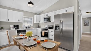 A modern kitchen with white cabinets, stainless steel appliances, and a dining area set for four. - Modern Hacienda | 3BR, Fenced Yard, Beach Gear, Dog-Friendly, Near Downtown (Sarasota)