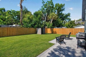 Ein Garten mit Holzzaun, Rasen und einer Grillplatz mit Sitzgelegenheiten.