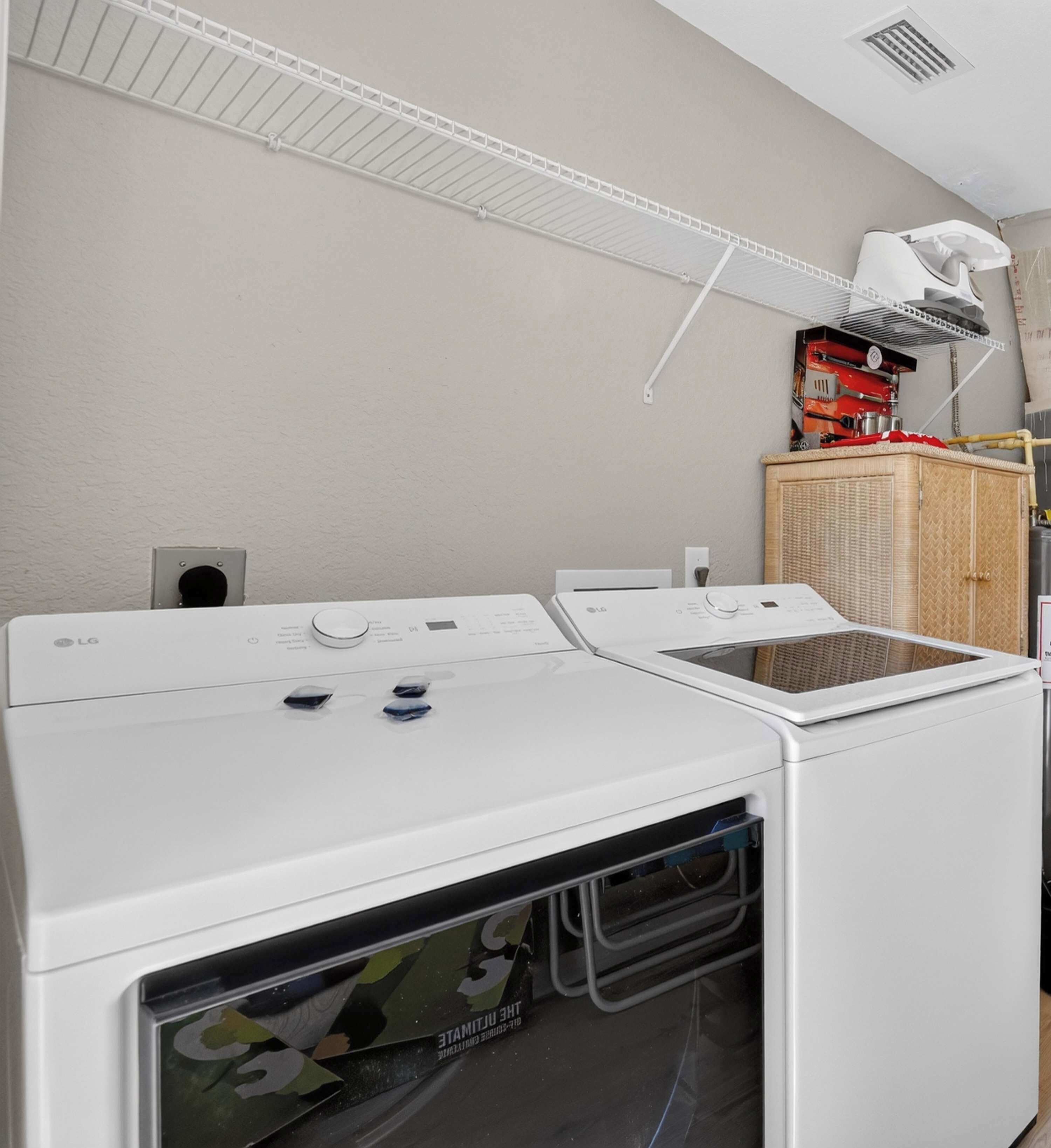 A laundry area with two white washing machines and a dryer, a white ceiling vent, and a wicker basket on a shelf.