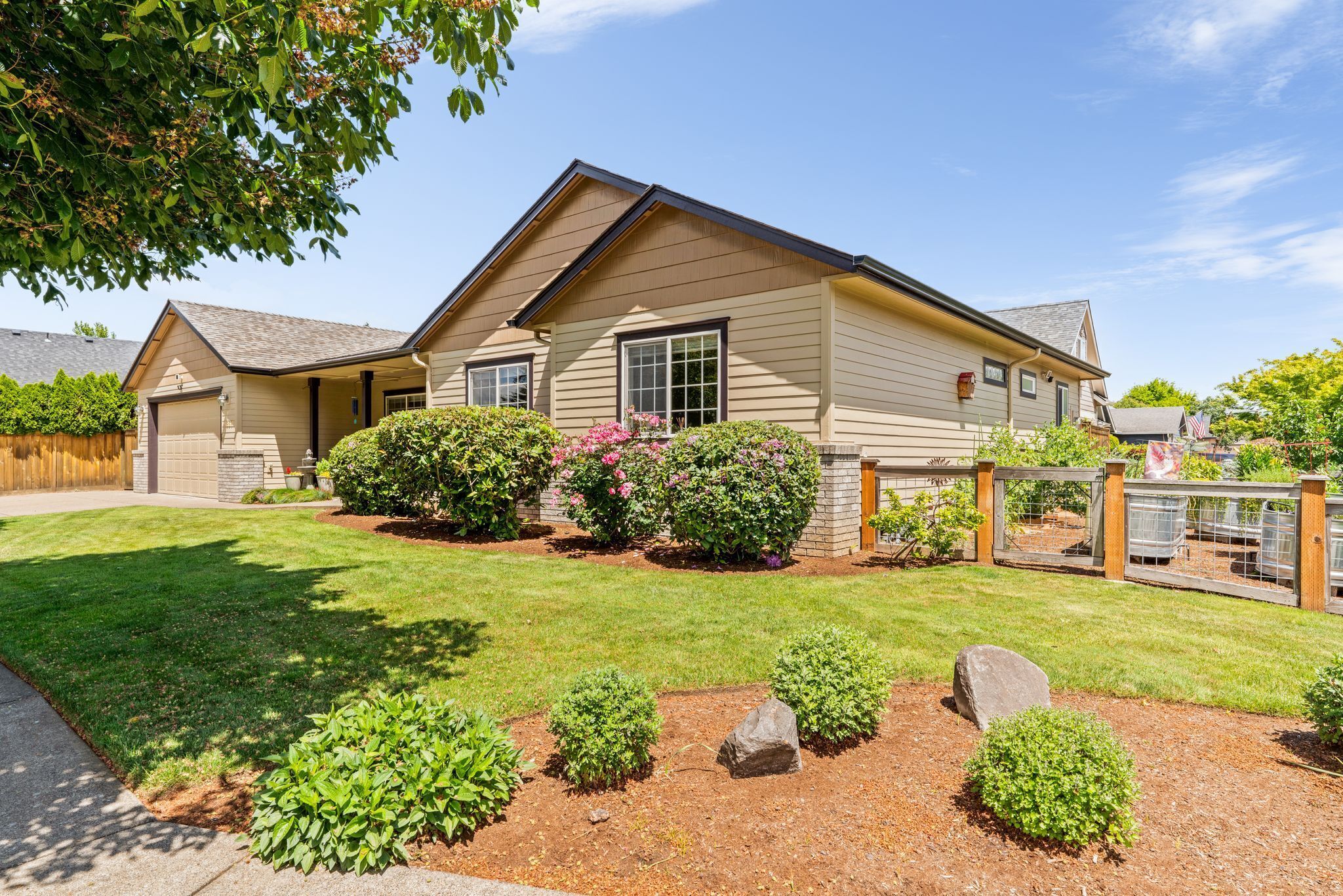 A single-story house with a garage, a well-maintained lawn, and a variety of shrubs and flowers.