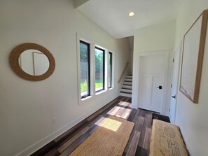 A hallway with a wooden floor, a mirror, and three windows.
