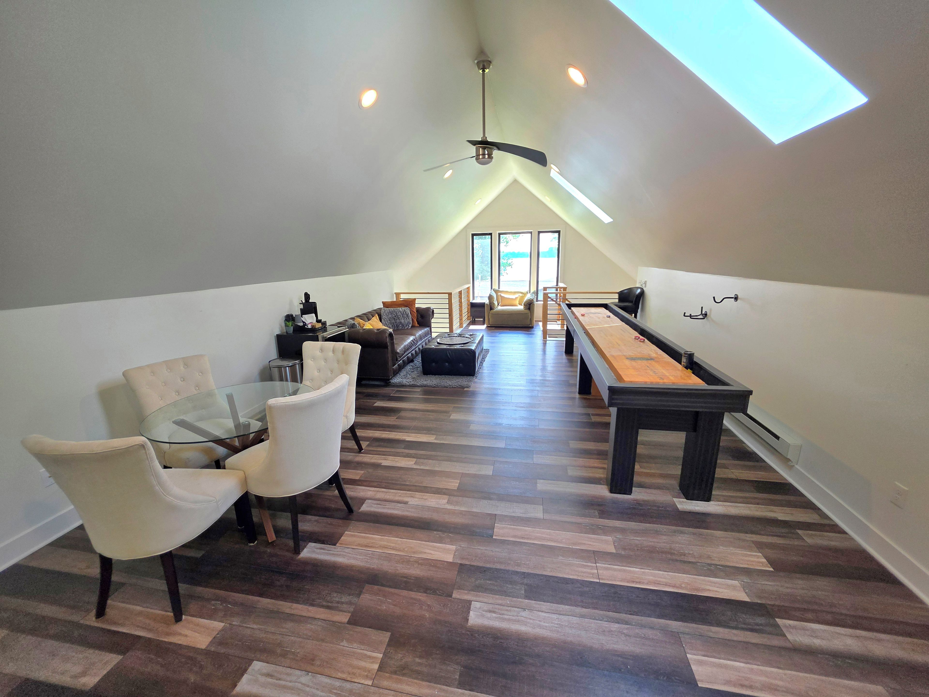 A loft-style living area with a dining table, chairs, a sofa, and a shuffleboard table.
