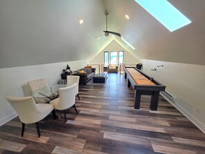 A loft-style living area with a dining table, chairs, a sofa, and a shuffleboard table.