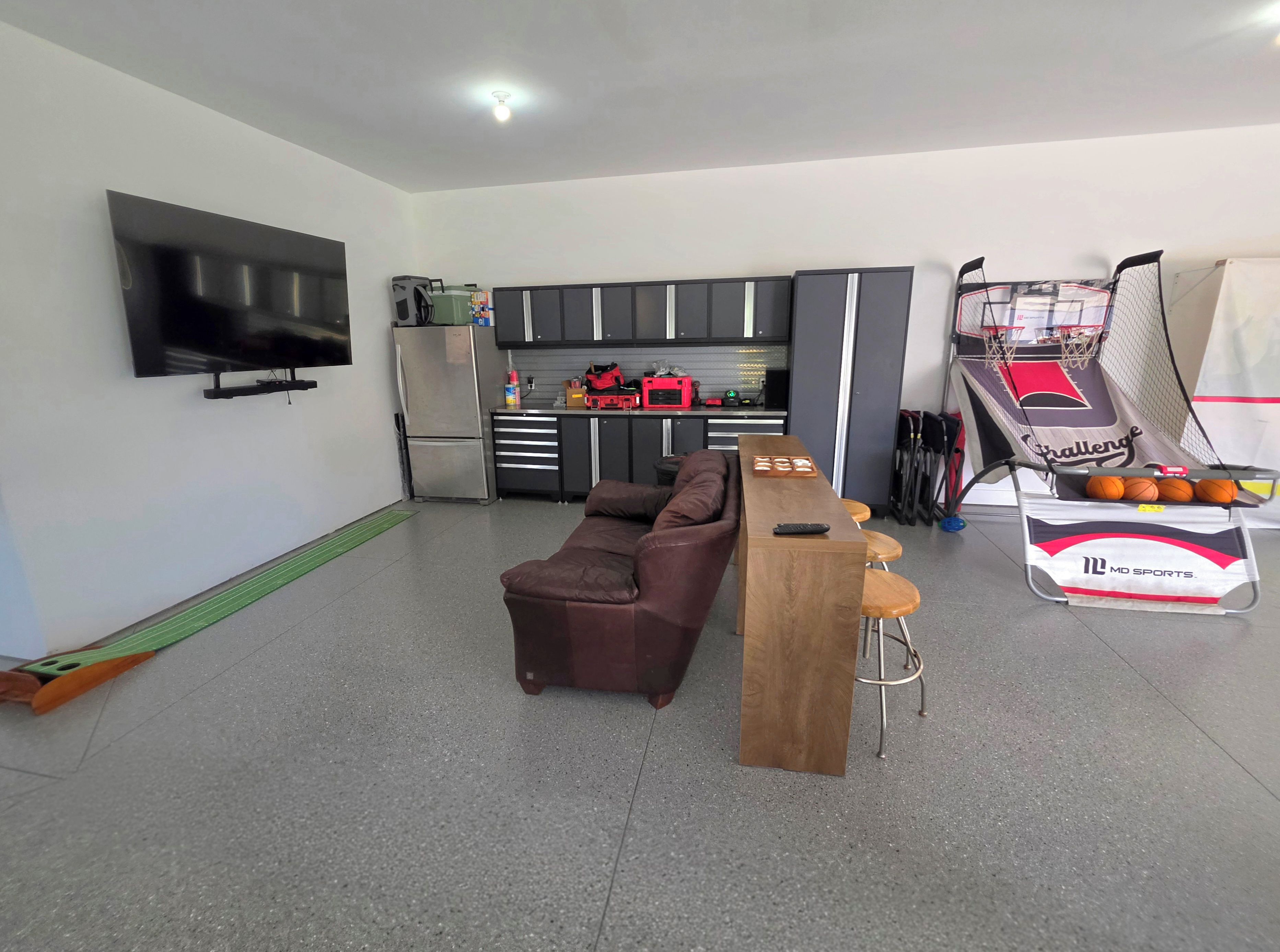 A modern living room with a flat-screen TV, a brown leather sofa, a wooden coffee table, and a basketball hoop.