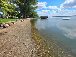 A lakeside view with a dock, clear water, and a grassy area with trees.