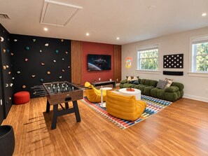 A modern living room with a foosball table, a sofa, and a colorful rug. - Hot-Tub, Pool, Golf, Pickleball, Basketball | Casa (Davie)