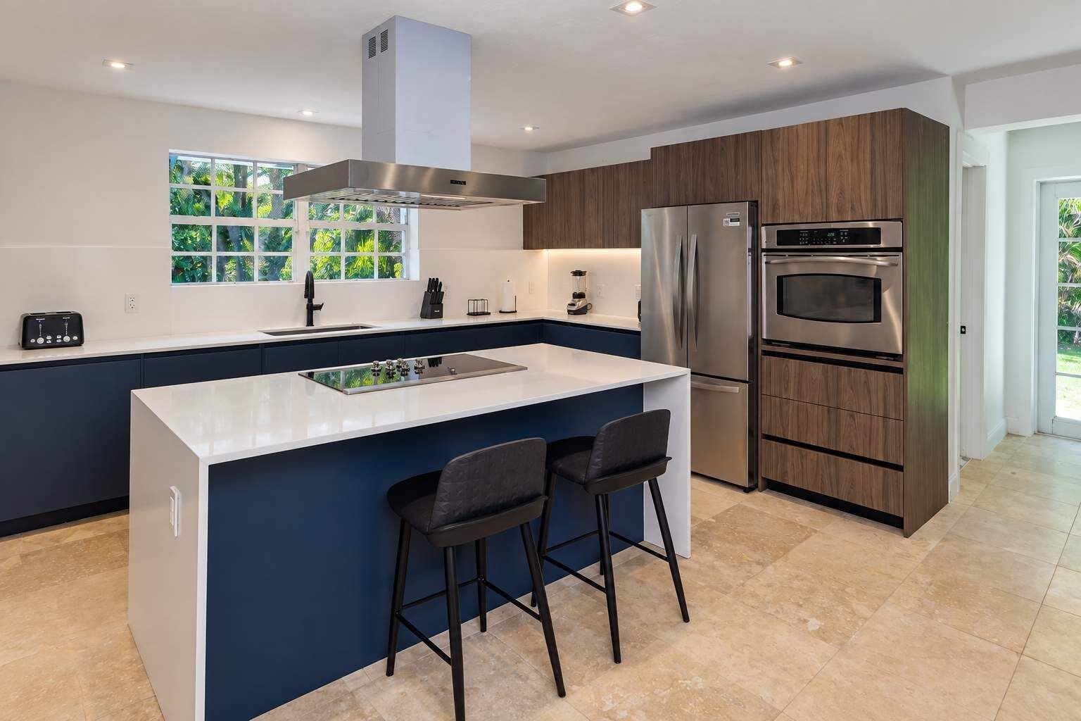 A modern kitchen with a large island, stainless steel appliances, and a view of greenery outside.
