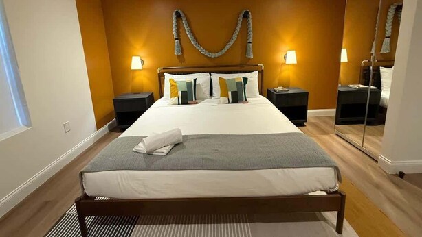 A modern hotel room with a large bed, bedside tables, a mirror, and a wall-mounted decorative piece. - 2-Acre Estate: Private Padel Court + Par-3 Golf (Davie)