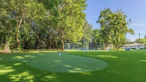 A golf course with a putting green, trees, and a fence. - 2-Acre Estate: Private Padel Court + Par-3 Golf (Davie)