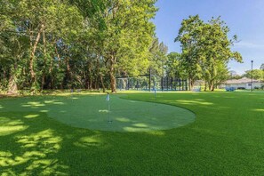Ein Golfplatz mit Putting Green, Bäumen und einem Zaun.