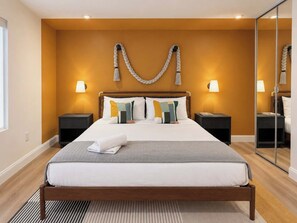 A hotel room with a bed, two bedside tables, a mirror, and a wall-mounted light fixture. - Hot-Tub, Pool, Golf, Pickleball, Basketball | Casa (Davie)