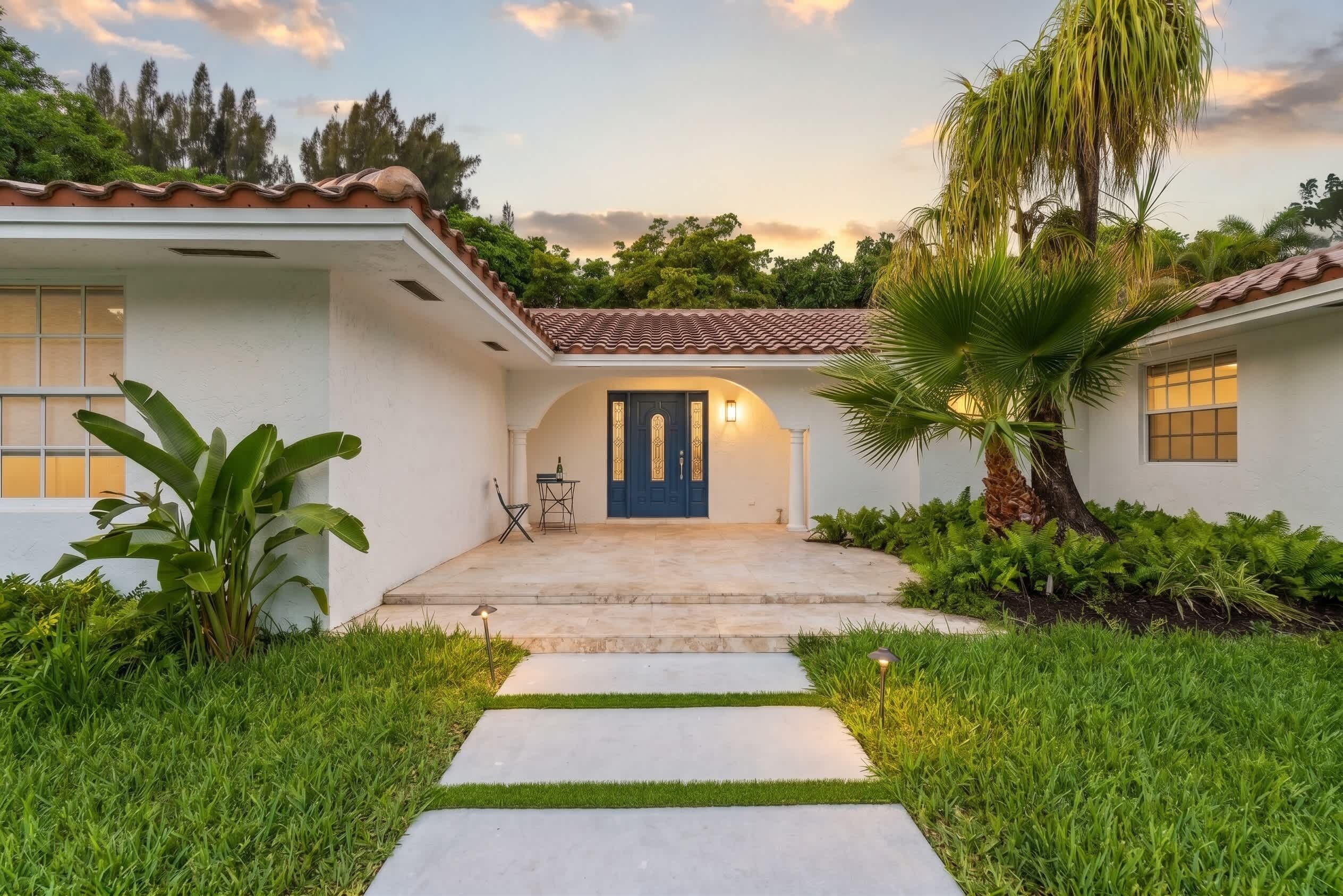 A house with a blue door, a tiled roof, and a pathway leading to the entrance.