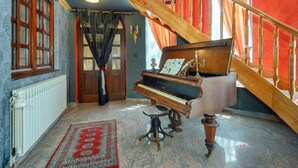 Un piano de cola en una habitación con una escalera roja, un tapete estampado y un amplio ventanal con cortinas.